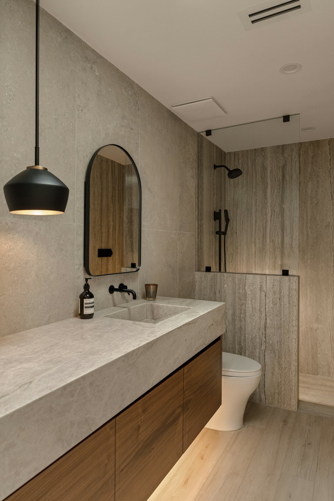 Bathroom with stone tile, wood vanity, and black fixtures